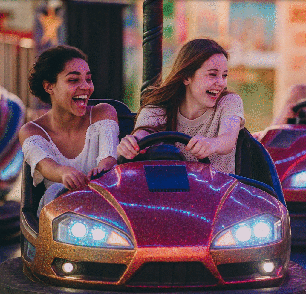 Två unga personer åker radiobilar på ett nöjesfält. De skrattar och ser ut att ha roligt, och karusellens färgglada ljus lyser upp kvällen.